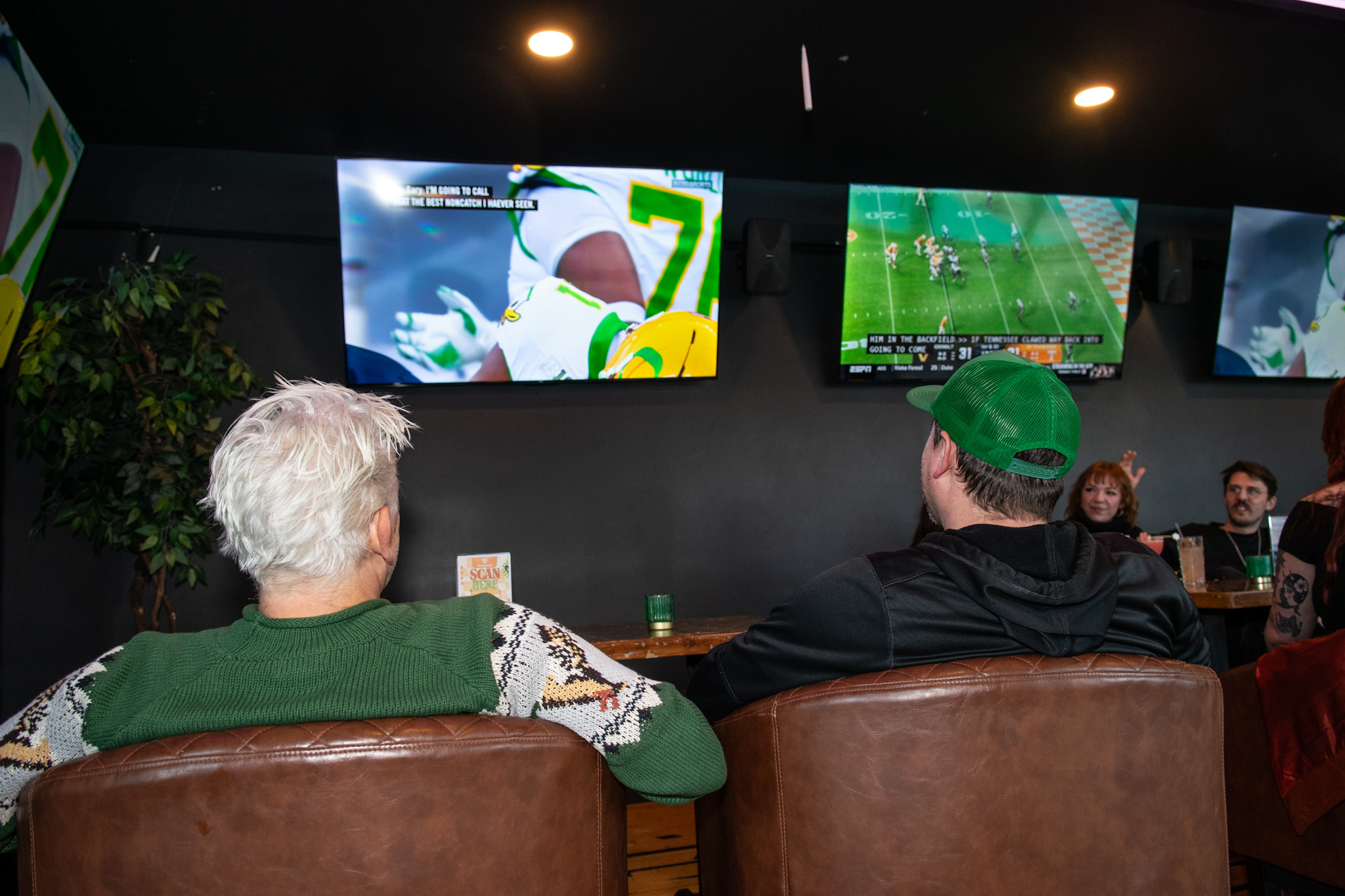 Football two middl age men watching Oregon Ducks football in the WonderLove sports lounge. Seated in luxury chocolate brown lounge chairs.