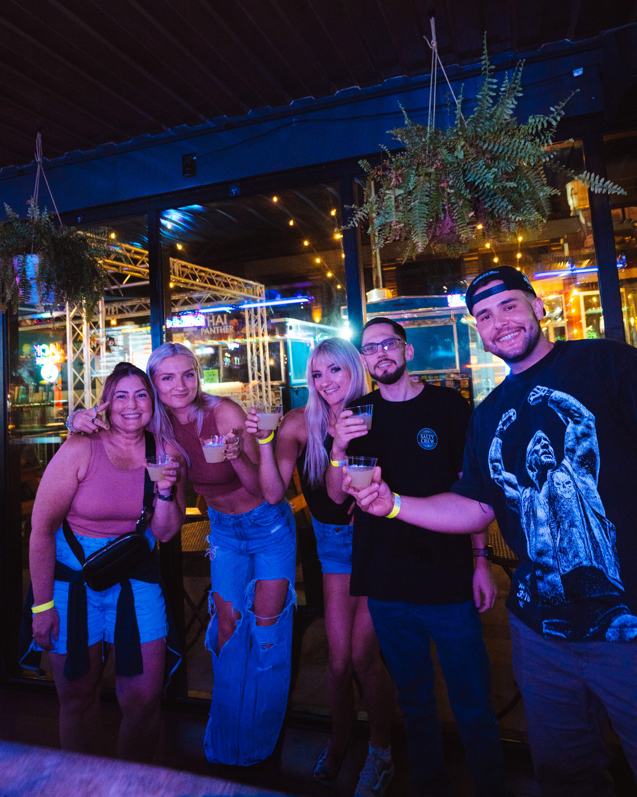 Night Life group of men and women cheers-ing with shot glasses at bar with plants
